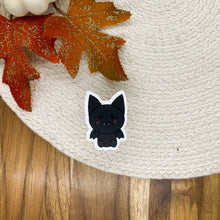 Load image into Gallery viewer, Cute black bat vinyl sticker with white border on woven placemat with autumn leaves