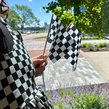 Load image into Gallery viewer, Person holding two black and white checkered racing flags in garden setting