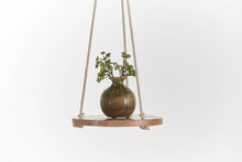 Load image into Gallery viewer, Round wooden hanging shelf with cotton rope holding brown glass vase with green plant
