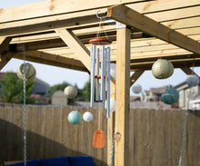 Load image into Gallery viewer, Large silver wind chime with metal tubes and wooden striker hanging from wooden pergola