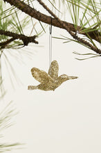 Load image into Gallery viewer, Gold glittered hummingbird Christmas ornament hanging from a pine tree branch