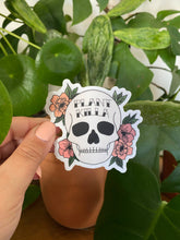 Load image into Gallery viewer, Hand holding Plant Killa skull sticker with pink flowers against green houseplants background