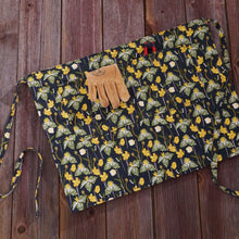 Load image into Gallery viewer, Black floral print gardening apron with tie strings and brown leather gloves on wooden surface