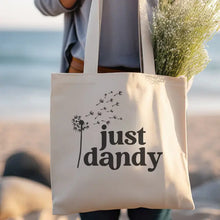 Load image into Gallery viewer, White canvas tote bag with 'just dandy' text and dandelion design being carried outdoors