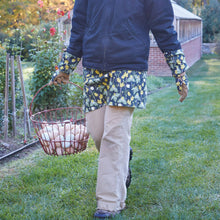 Load image into Gallery viewer, Person wearing floral patterned gardener's half apron while collecting eggs in wire basket outdoors