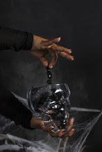 Load image into Gallery viewer, Crystal skull-shaped glass pot holding black Halloween candy against dark moody background