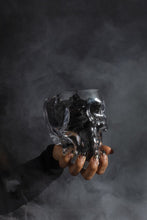 Load image into Gallery viewer, Clear glass skull-shaped planter pot held against dramatic smoky dark background