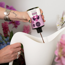 Load image into Gallery viewer, Person pouring liquid plant food concentrate from pink bottle into white watering can