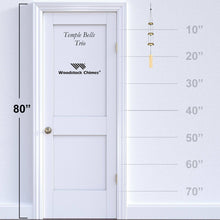 Load image into Gallery viewer, Woodstock Temple Bells Trio wind chimes shown hanging next to door with measurement scale