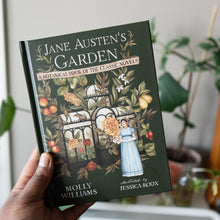 Load image into Gallery viewer, Hand holding Jane Austen's Garden hardcover book with botanical illustration cover featuring greenhouse and flowers