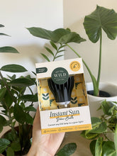 Load image into Gallery viewer, Hand holding We The Wild Instant Sun Grow Bulb package with black LED bulb visible inside