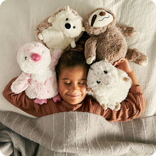 Load image into Gallery viewer, Child smiling while surrounded by four plush animal heating pads including hedgehog, sloth, and bunny