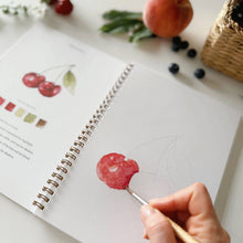 Load image into Gallery viewer, Hand painting red watercolor fruit in spiral-bound art workbook with fresh fruits nearby