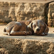 Load image into Gallery viewer, Bronze-colored sleeping dog statue lying on stone surface in garden setting