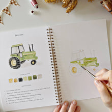 Load image into Gallery viewer, Open watercolor workbook showing green tractor painting tutorial with color palette and brush in hand