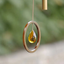 Load image into Gallery viewer, Bronze wind chime with wooden oval frame and golden crystal teardrop pendant hanging outdoors