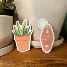 Load image into Gallery viewer, Two coral-colored stickers featuring potted succulent plant and vintage motel keychain with plants quote