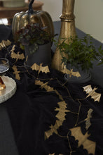Load image into Gallery viewer, Gold metallic bat garland draped across a black Halloween tablescape with pumpkin decor.