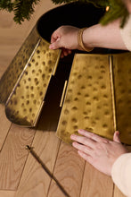 Load image into Gallery viewer, Hands assembling a hammered gold metal Christmas tree collar around a tree base