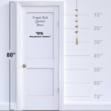 Load image into Gallery viewer, Woodstock Temple Bells Quintet wind chimes with brass bells hanging beside white door with measurement scale