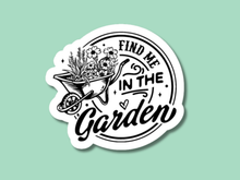 Load image into Gallery viewer, Black and white circular sticker with wheelbarrow full of flowers reading Find Me In The Garden