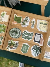 Load image into Gallery viewer, Collection of plant-themed stickers displayed in wooden compartment box including monstera leaf design