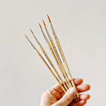 Load image into Gallery viewer, Hand holding five wooden watercolor paintbrushes with fine pointed tips and natural wood handles