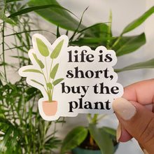 Load image into Gallery viewer, Hand holding white sticker with plant illustration reading 'life is short, buy the plant'