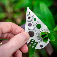 Load image into Gallery viewer, Stainless steel leaf-shaped foraging tool with decorative cutouts held against green foliage background