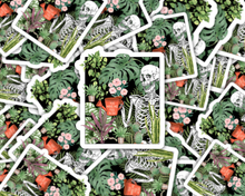 Load image into Gallery viewer, Skeleton surrounded by plants sticker with text 'You Make Me Feel Alive' on terracotta pot
