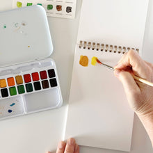 Load image into Gallery viewer, Artist painting yellow watercolor swatches on a spiral-bound watercolor paper pad