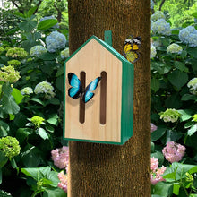 Load image into Gallery viewer, Wooden butterfly house with green trim mounted on tree trunk surrounded by hydrangeas