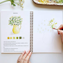 Load image into Gallery viewer, Open watercolor workbook showing daisy painting tutorial with yellow pitcher, color palette, and painting instructions