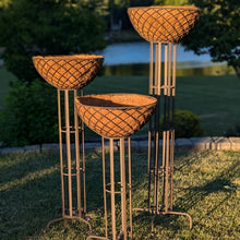 Load image into Gallery viewer, Three tiered copper-colored woven basket planters on tall metal stands in garden setting