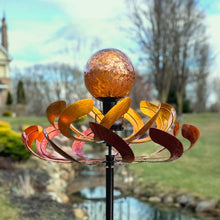 Load image into Gallery viewer, Copper and bronze wind spinner with textured glass orb mounted on black pole in garden setting