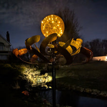 Load image into Gallery viewer, Illuminated bronze metal orb wind spinner with LED lights in evening garden setting