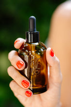 Load image into Gallery viewer, Hand holding amber glass dropper bottle with plant fertilizer serum against green background