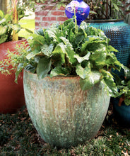 Load image into Gallery viewer, Anamese Luna Egg Planter with weathered verdigris finish displayed outdoors with lush green plants