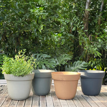 Load image into Gallery viewer, Four circular planters in different colors arranged on wooden deck with lush greenery background