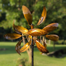 Load image into Gallery viewer, Golden copper wind spinner with curved petal blades mounted on black pole in garden setting