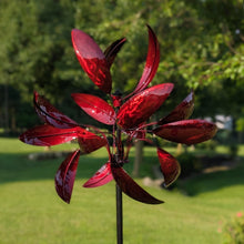 Load image into Gallery viewer, Red metallic wind spinner with flower-shaped blades in garden setting