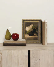 Load image into Gallery viewer, Framed magnolia flower oil painting displayed on a wooden sideboard with books and fruit