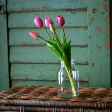 Load image into Gallery viewer, Four pink tulips in clear glass jar on wicker basket against weathered green wood background