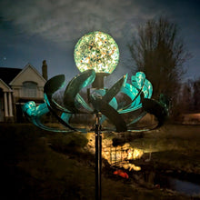 Load image into Gallery viewer, Illuminated metal wind spinner with glowing orb center spinning in twilight garden setting