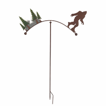 Load image into Gallery viewer, Metal garden stake with Bigfoot silhouette and evergreen trees balancing on curved top rod