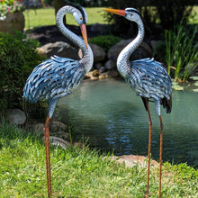 Load image into Gallery viewer, Two decorative metal heron sculptures with blue-gray feathers standing beside garden pond