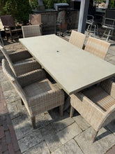 Load image into Gallery viewer, Seven-piece outdoor wicker dining set with rectangular grey stone-top table on stone patio