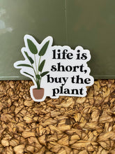 Load image into Gallery viewer, White vinyl sticker with plant illustration saying 'life is short, buy the plant' on wood chips