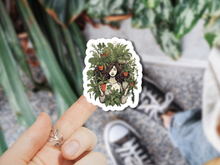 Load image into Gallery viewer, Hand holding decorative sticker featuring woman with flowing hair surrounded by potted plants and greenery