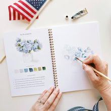 Load image into Gallery viewer, Hands painting watercolor hydrangeas in spiral-bound art workbook with American flag nearby